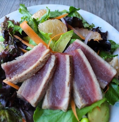 Close up side angle of seared ahi tuna steak served over mesclun salad with avocado and grapefruit segments.