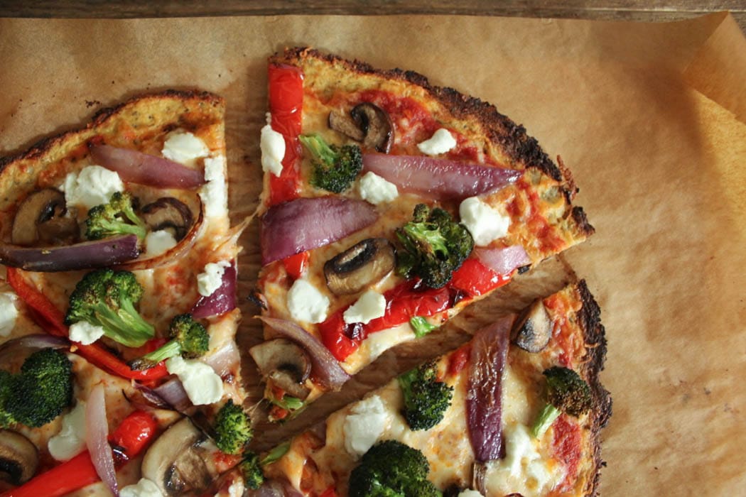 Sliced cauliflower crust pizza with roasted vegetables and goat cheese.