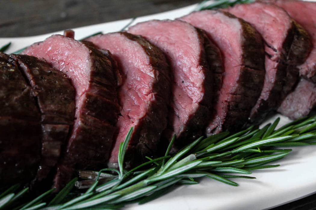 Slice slow-roasted beef tenderloin with rosemary on a platter.