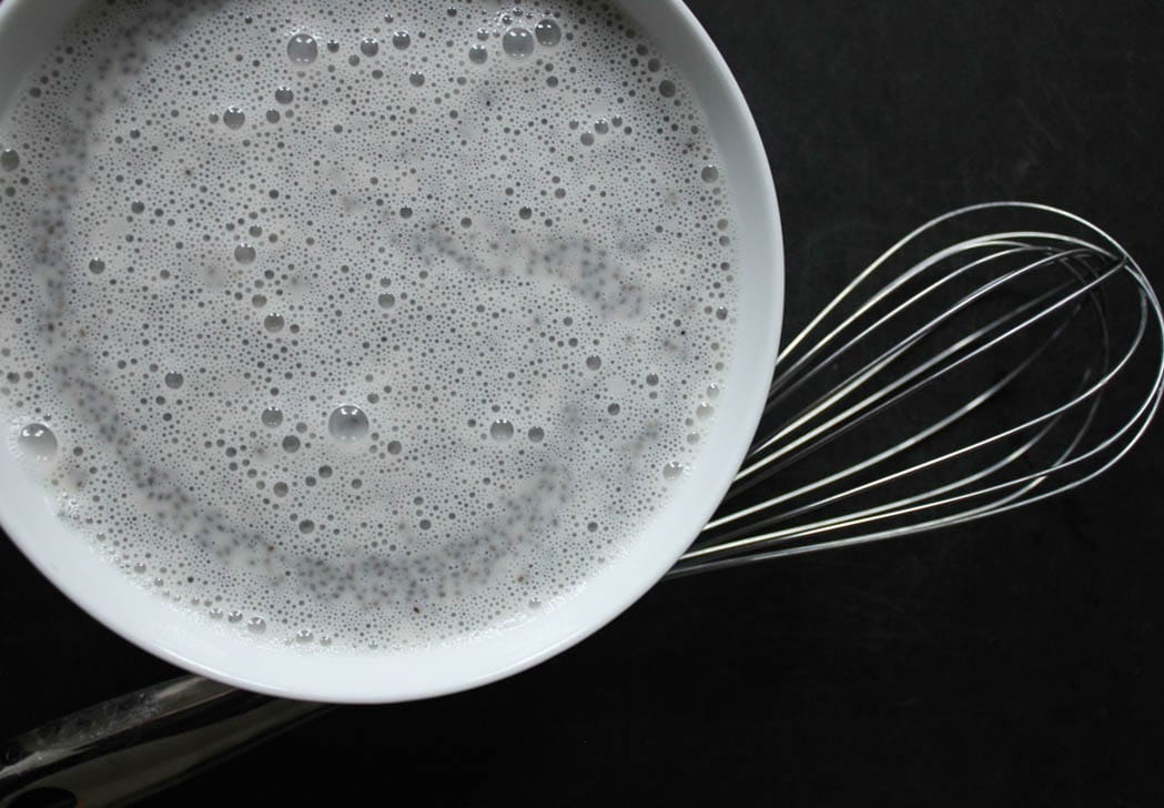 Bowl with frothy almond milk and chia seeds accompanied by a whisk.