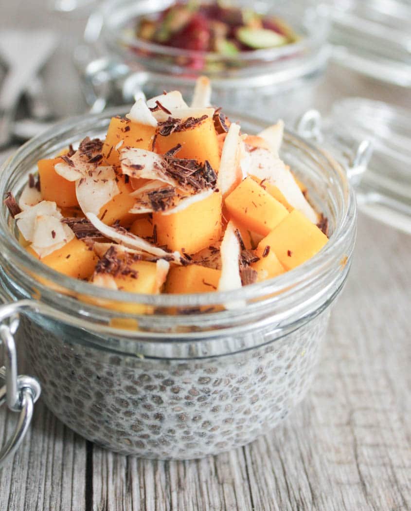 Side view of clear weck jar filled with chia seed pudding and topped with diced mango, shaved coconut and chocolate.