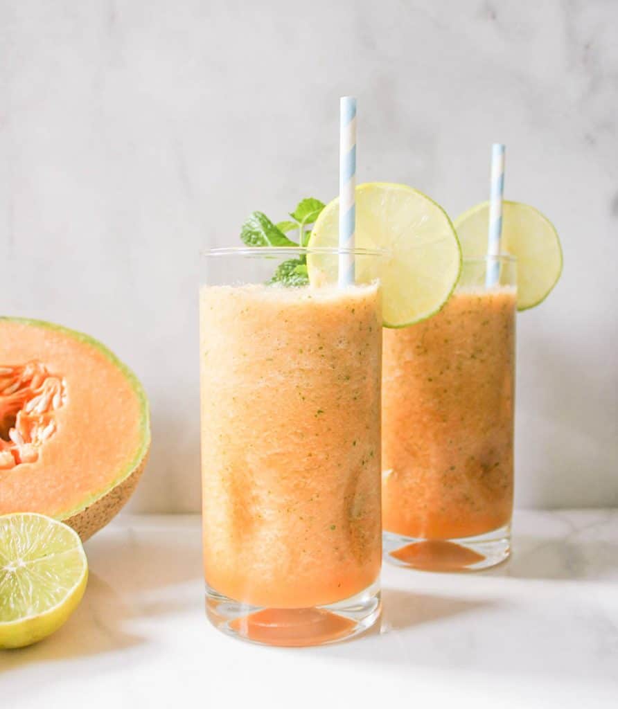 Two glasses of Cantaloupe Coolers garnished with slices of lime. 