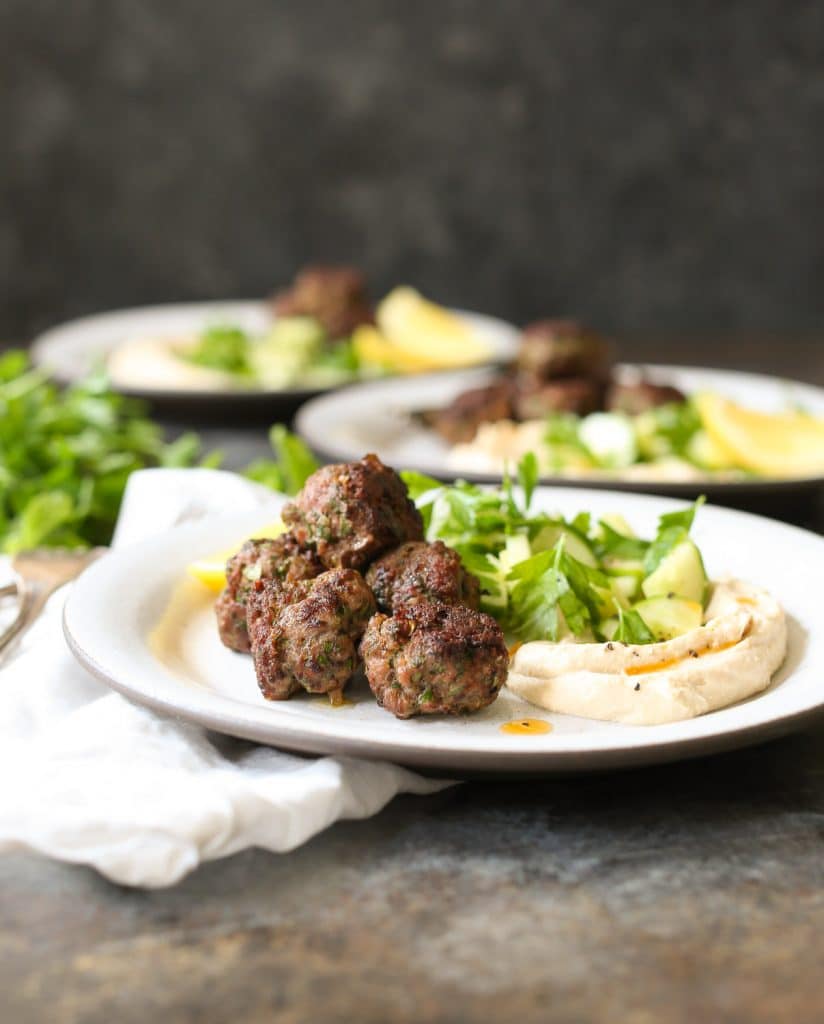 Three plated servings of lamb kofta with hummus and herbs.