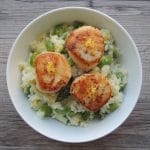 Bowl of spring vegetable risotto topped with three seared scallops.