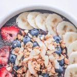 Tropical Acai Bowl topped with banana slices, strawberry slices, chia seeds, blueberries, granola, and nuts.