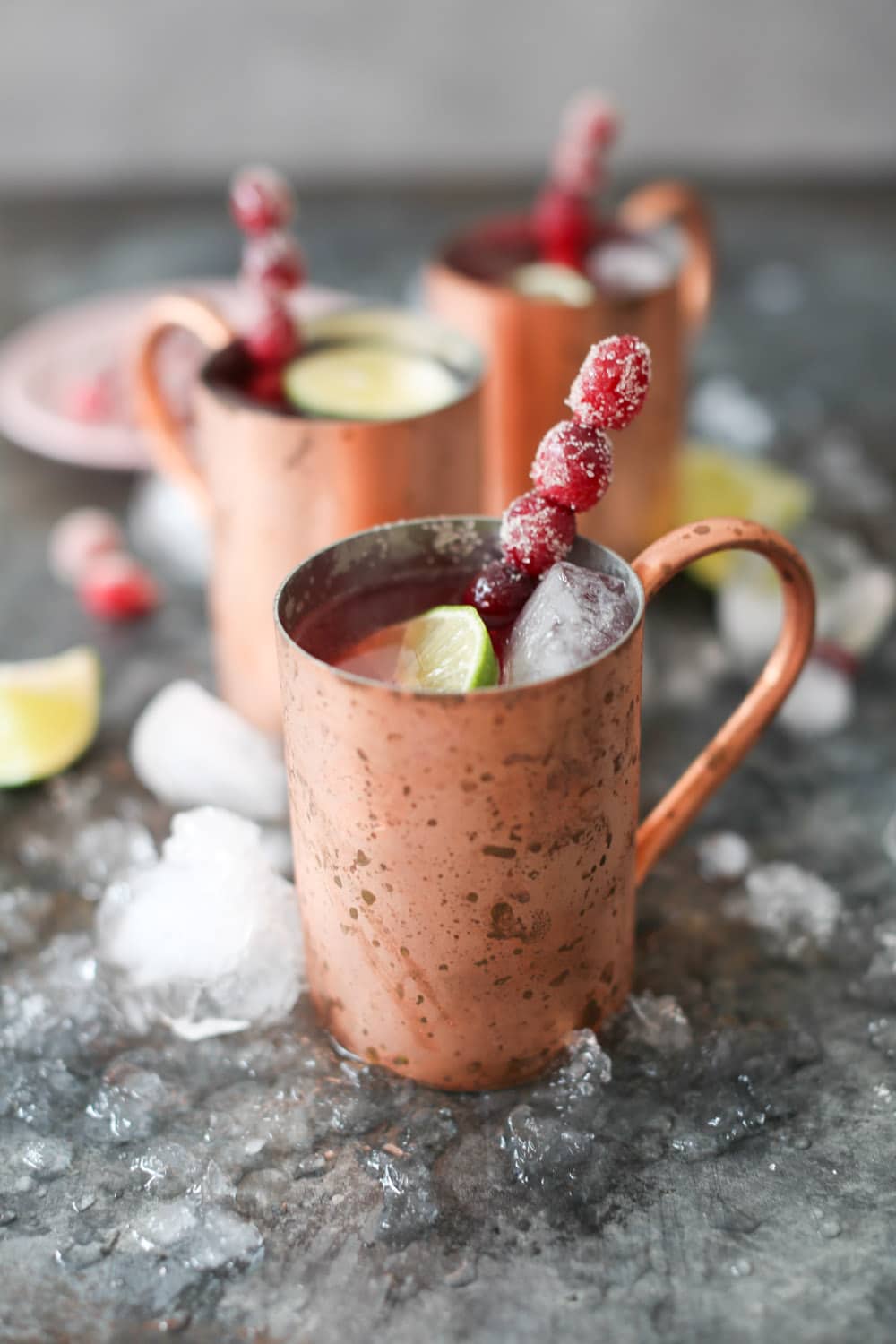Close-up side view of a chilled Cranberry Moscow Mule garnished with a cranberry swizzle stick and a lime round. 
