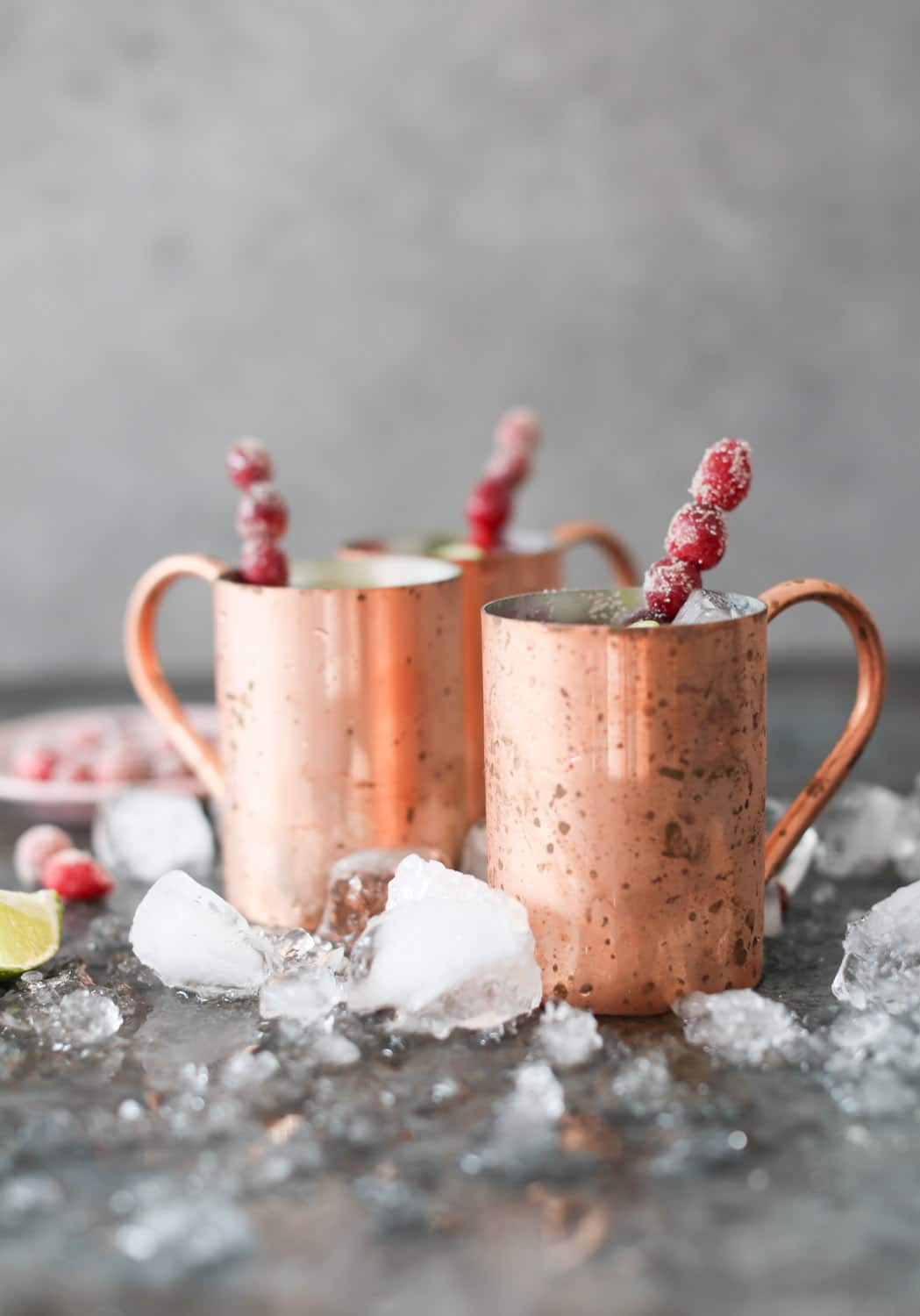 SIde view of Holiday Moscow Mules in copper mugs with sugared cranberry swizzle sticks.