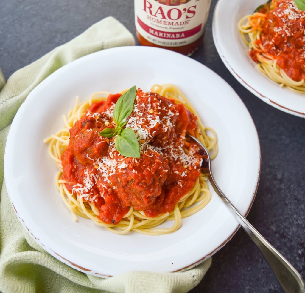 Two bowls of homemade meatballs over spaghetti with marinara sauce and basil garnish.