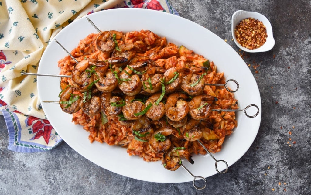 Platter of orzo in tomato basil sauce with grilled zucchini topped with skewers of grilled balsamic-marinated shrimp.