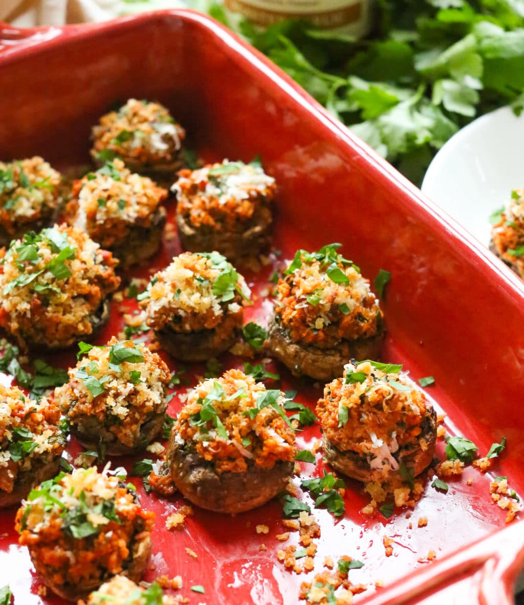 Side angle shot of a baking dish of bite-size stuffed mushroom with a small appetizer plate peeking in on the right side. 