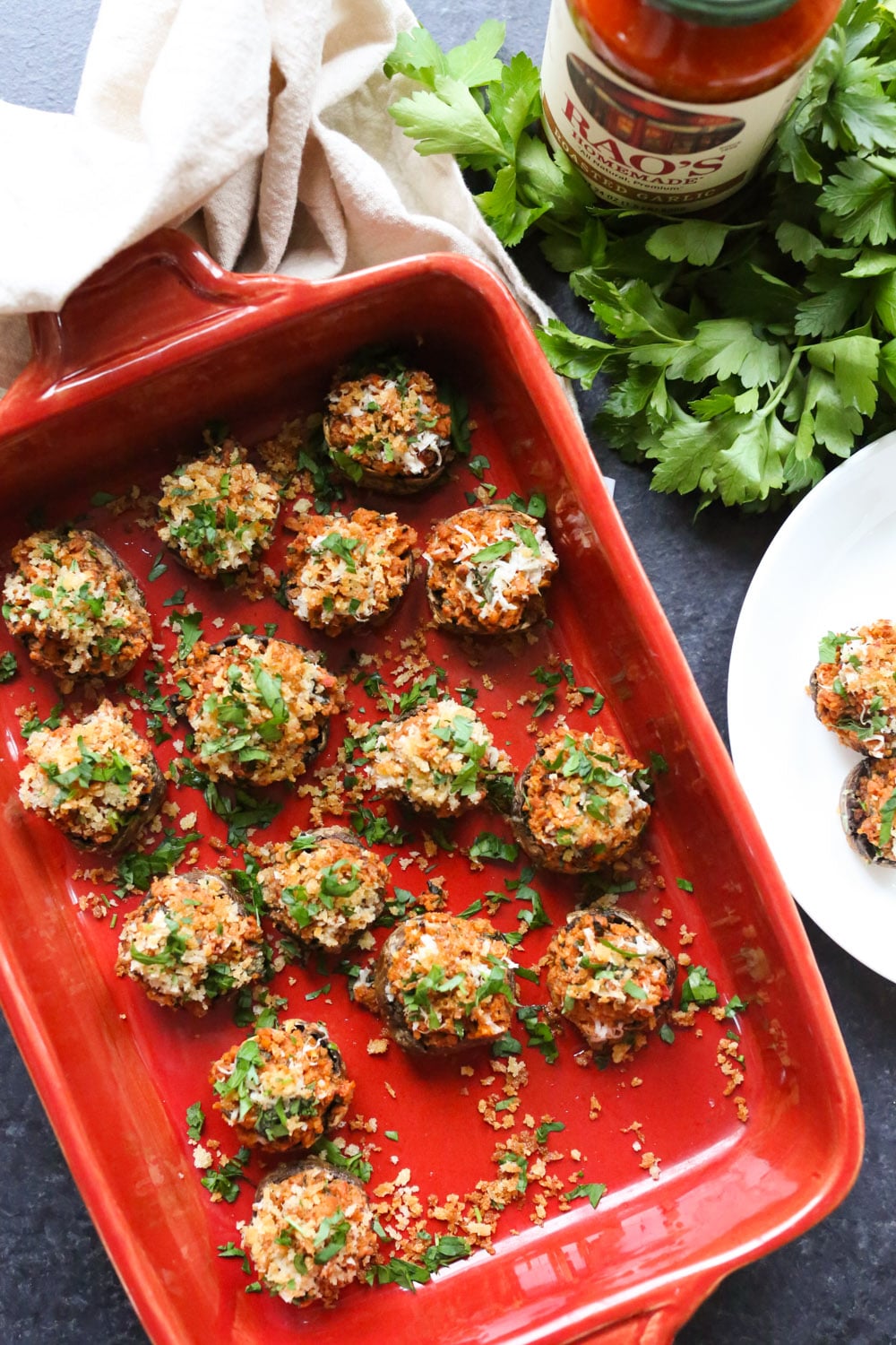 Overhead shot of stuffed mushrooms in a baking dish with a jar of Rao's Homemade tomato sauce and parsley. 