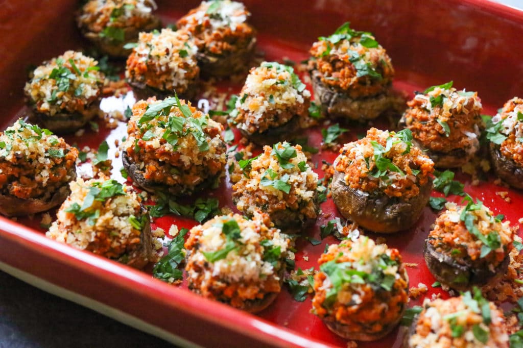 Side view of a tray of bite-size sausage stuffed mushrooms topped with parsley.
