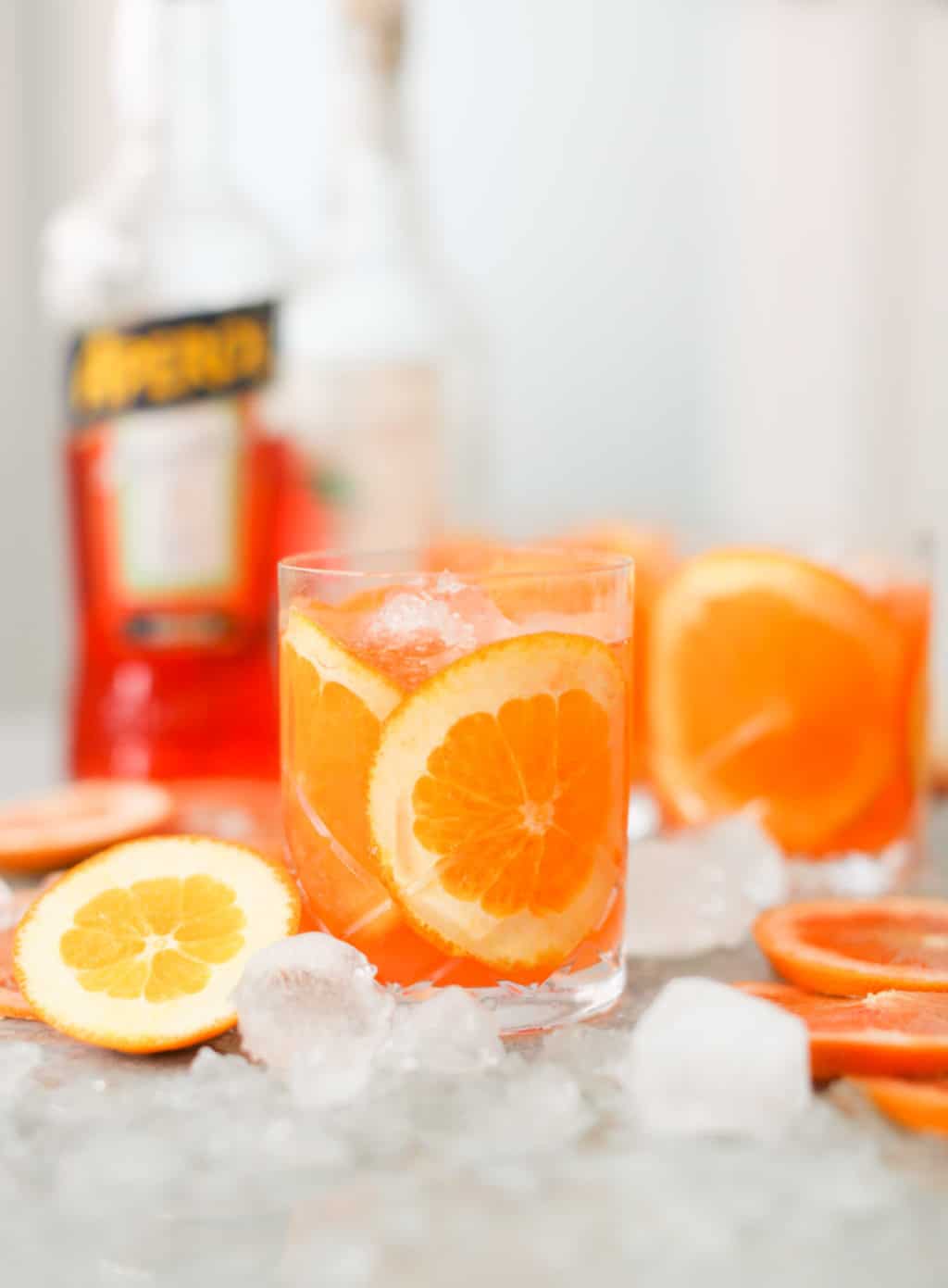 A short glass of Aperol Grapefruit Margarita with slices of grapefruit inside and surrounding the glass on a bed of ice. 