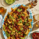 Overhead shot of a platter of nachos with small bowls of toppings and open beer bottles